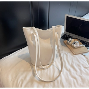 Detailed close-up of white crocodile pattern bucket bag with thin straps on soft bedding