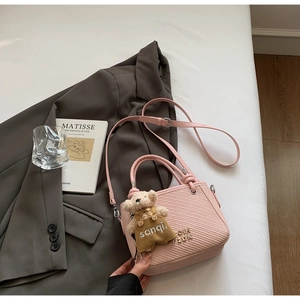 Detail of pink bucket bag with woven texture, metal logo and a cute bear charm accessory