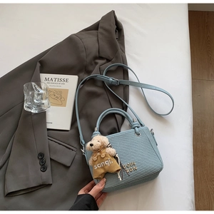 Detail of light blue bucket bag with woven texture, metal logo and dog doll charm