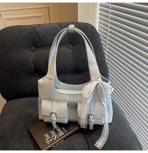 Dettaglio della borsa tote azzurra con tasche frontali e decorazione con fiocco in pizzo