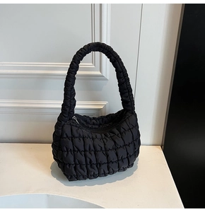 Detalle de bolso de hombro acolchado negro con correas plisadas y textura de cuadrícula