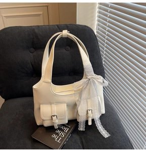 Dettaglio ravvicinato della borsa tote bianco crema con fiocco in pizzo e fibbie argentate