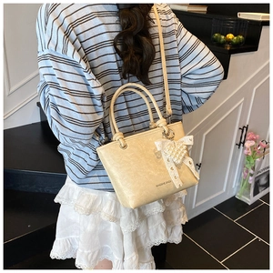Detail of beige bucket bag with pearl heart charm and lace bow on textured PU leather