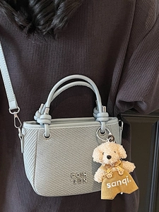 Light blue textured bucket bag with metal logo and cute plush puppy charm accessory