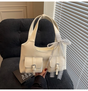 Dettaglio borsa crema con due tasche dotate di fibbie metalliche e decorazione a fiocco