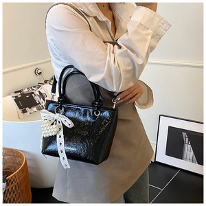 Detail view of glossy black bucket bag with a white lace bow and a heart pearl charm