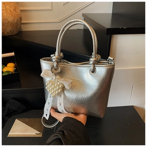 Détail du sac à main plissé argenté avec breloque cœur en perles et nœud en dentelle blanche