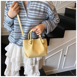Detail view of a bright yellow woven leather tote bag with a knotted strap on a model