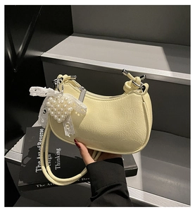 Close-up of a yellow dumpling bag with lace bow and pearl heart charm detail