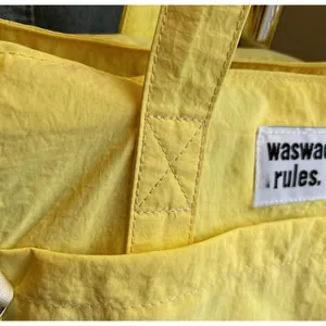 Detail of yellow canvas tote showing reinforced X-shaped stitching and fabric brand label