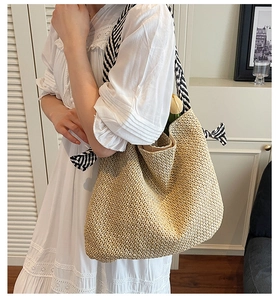 Detail of woven straw tote bag featuring black and white striped ribbon shoulder straps