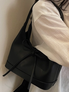 Minimalist black PU leather tote bag with bow detail worn by a model in casual attire