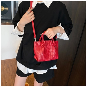 Detail of red woven bucket bag with knot handles and adjustable crossbody strap on model