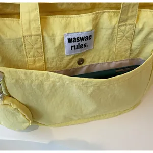 Detail view of yellow nylon tote bag front pocket with button and green tablet inside