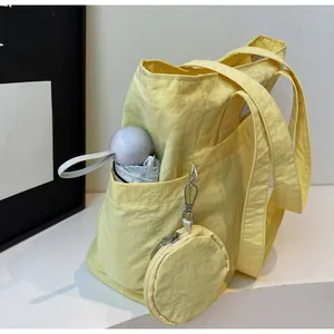 Detail of cream yellow nylon tote bag side pocket holding a folding umbrella with mini pouch