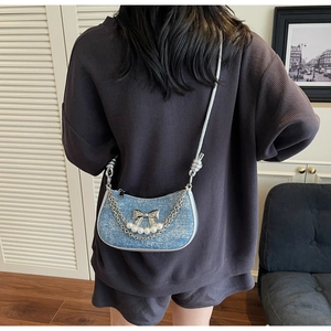 Detail of light blue denim crescent bag with metallic bow and pearl chain decoration