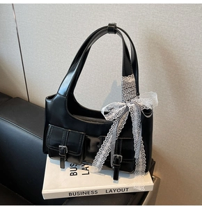 Dettaglio borsa tote in ecopelle nera con fiocco in pizzo e due tasche anteriori