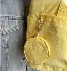 Detail of yellow nylon round coin pouch with silver carabiner and zipper on a bag