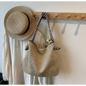 Detail of woven straw tote bag with striped fabric strap and decorative ribbon bow