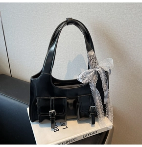 Dettaglio borsa tote nera in vernice con fibbie argentate e accessorio fiocco in pizzo bianco