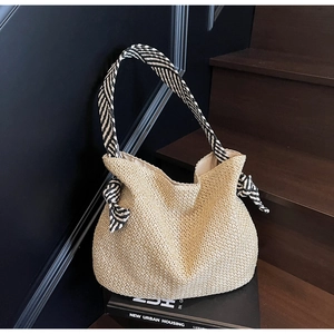 Detailed texture of straw woven tote bag featuring black and white striped ribbon shoulder strap