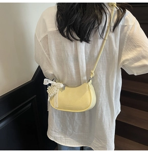 Detail view of yellow crescent bag featuring glossy PU leather and heart pearl lace charm