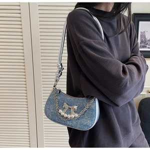 Detail of blue denim shoulder bag with silver chain, white pearls and metal bow