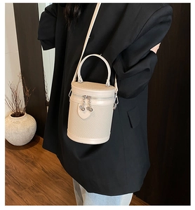 Dettaglio di una borsa a secchiello beige intrecciata con manico in pelle e doppie cerniere