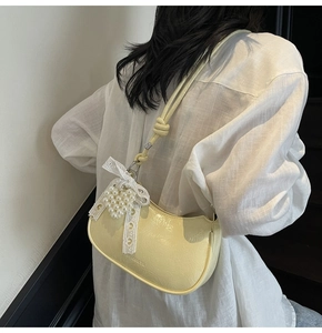 Detail of light yellow textured croissant bag with pearl lace bow charm on model