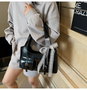Dettaglio borsa tote in pelle nera lucida con tasche e fiocco in pizzo bianco decorativo