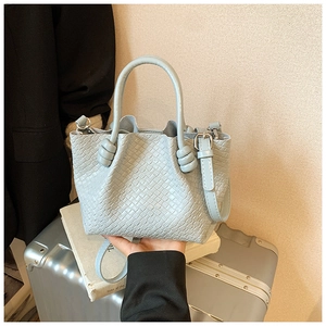 Close-up of light blue woven bucket bag featuring decorative handle knots and silver hardware