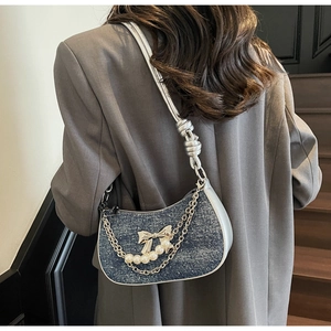 Detail of blue denim hobo bag with silver bow charm, pearls and chain strap over grey blazer