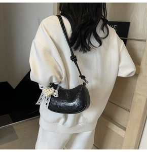 Detail of black patent leather hobo bag with lace bow and pearl heart charm on model