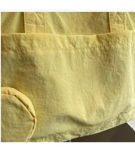 Detailed close-up of yellow wrinkled nylon fabric with white logo label on tote bag