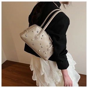 Side view of beige shoulder bag with pearl and star rivet details shown on a model