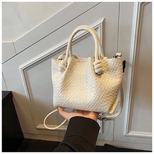 Detail of creamy white woven bucket bag with unique knot handle design and adjustable strap