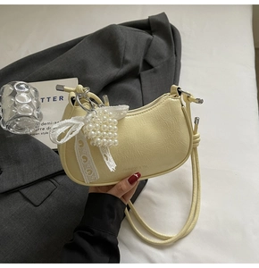 Detail of light yellow crescent bag featuring pearl charms and a white lace bow accent