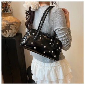 Detail of black glossy patent leather shoulder bag with decorative pearls and metal stars