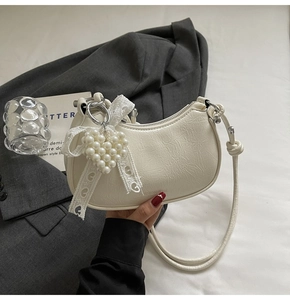 Detail of white crescent bag featuring crinkled leather and large pearl heart charm