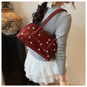 Detail of dark red Boston bag with star rivets and pearls held by a model