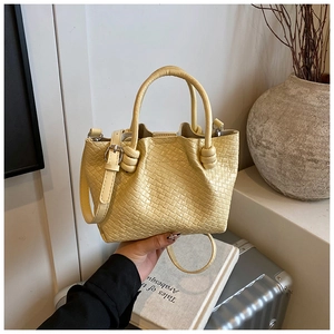 Close-up of pale yellow woven bucket bag featuring detailed Intrecciato texture and strap