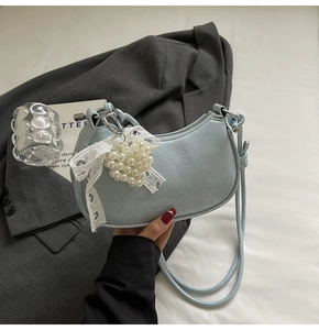 Detail of light blue crescent bag with vintage texture and pearl lace bow charm