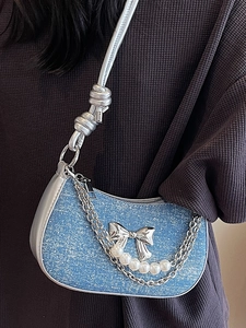 Blue denim mini underarm bag with silver bow and pearl chain worn by a model