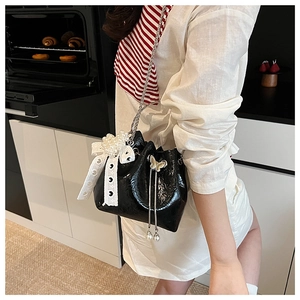 Détail d'un sac seau noir brillant avec chaîne en perles et nœud décoratif élégant