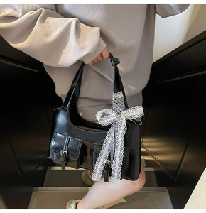 Dettaglio borsa tote in pelle nera lucida con grande fiocco in pizzo e fibbie