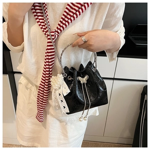 Détail du sac seau noir brillant avec poignée en métal, chaîne et breloque en perles et dentelle