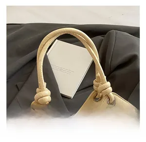 Detail der cremefarbenen Leder-Eimertasche mit Knotengriff und Perlenanhänger-Deko