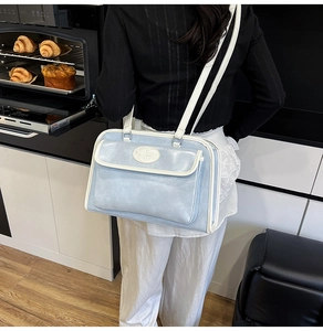 Detail of light blue tote bag with white piping, front flap pocket and oval logo plaque