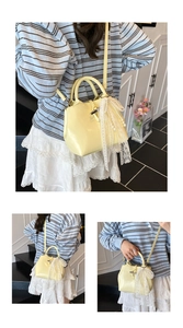Detail of light yellow bucket bag with lace bow and pearl pendant on shiny leather