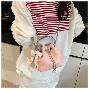Détail du sac seau rose à cordon avec poignée en métal, fermoir nœud et breloque en perle